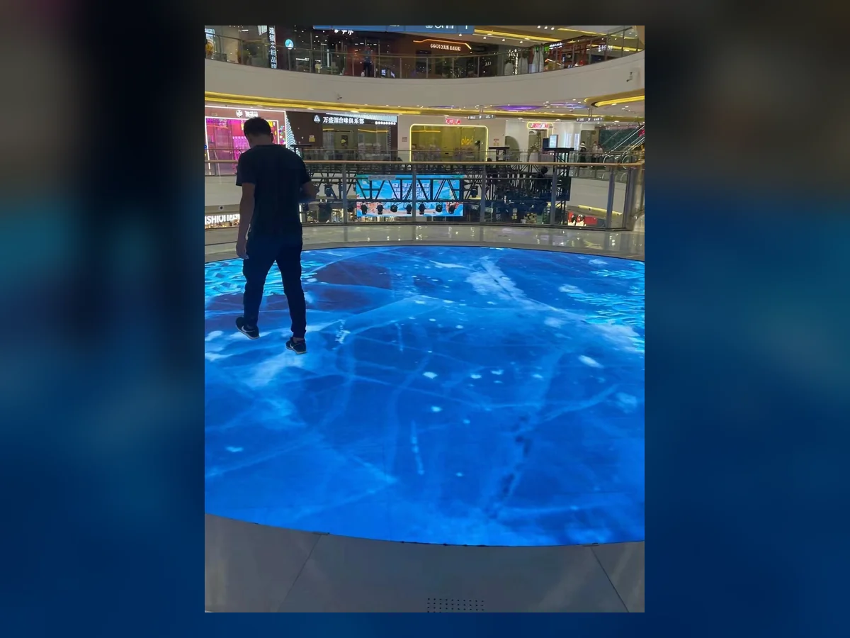 Person walking across a circular LED floor display in a shopping venue